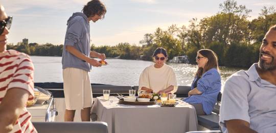 Groupe d’amis savourant un repas en toute détente sur le pont du bateau au coucher du soleil.